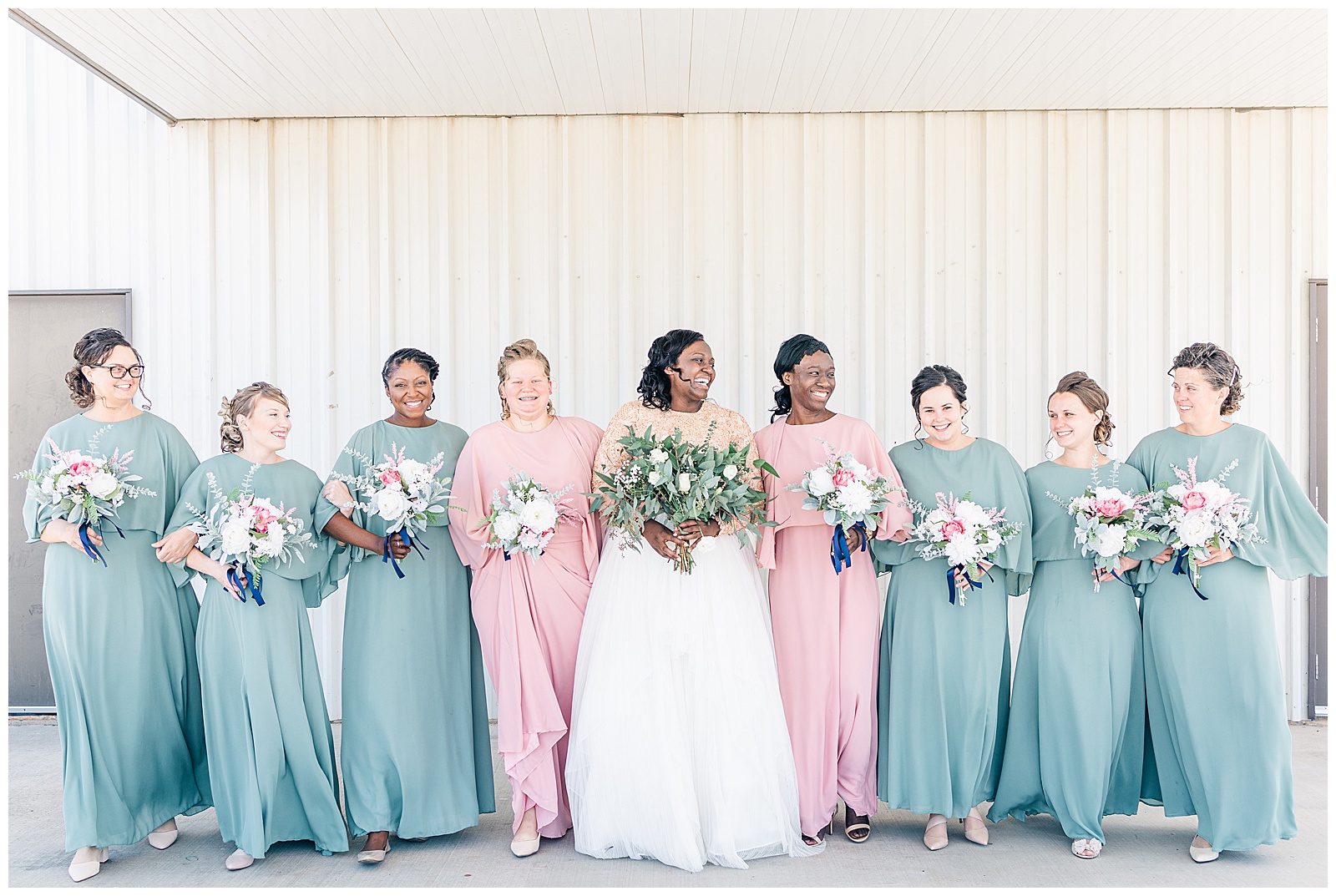 Bride and bridesmaids walking towards camera and laughing in blush and sage green dresses
